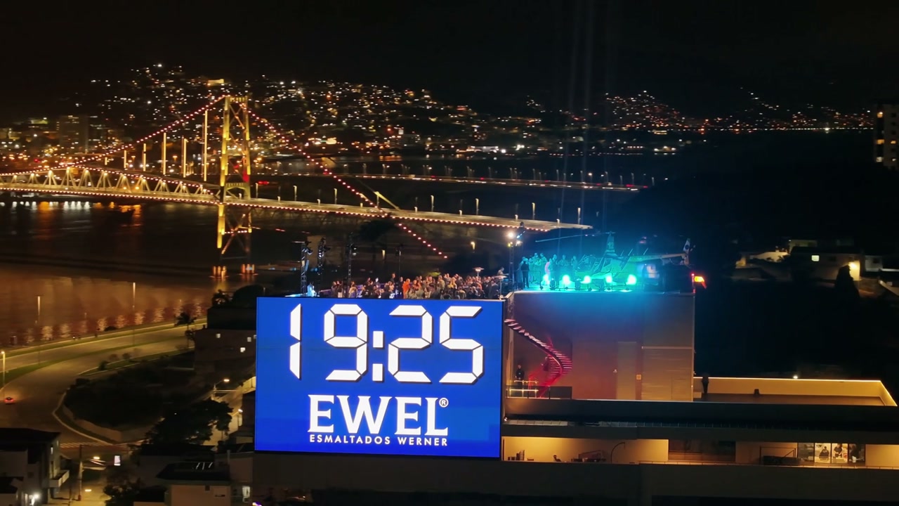 Megatela Floripa Square iluminada à noite sobre o skyline de Florianópolis com a Ponte Hercílio Luz ao fundo